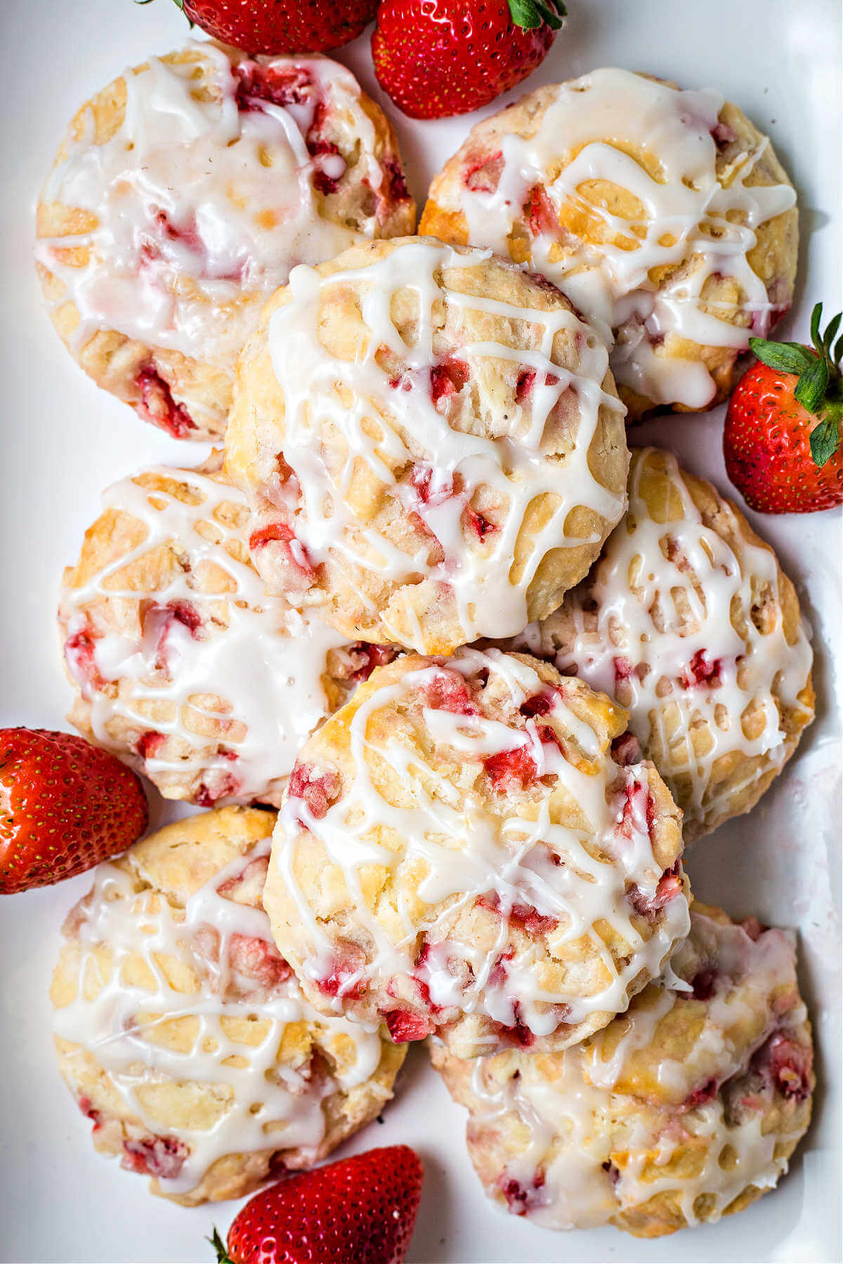 a platter of strawberry biscuits drizzled with a glaze and with whole strawberries garnishing the dish.