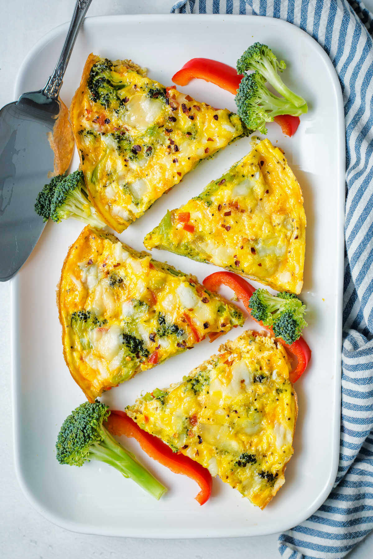 servings of vegetable frittata on a white platter garnished with broccoli florets and red bell pepper strips.