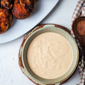 a bowl of Alabama white BBQ sauce on a table with a checked napkin and wooden spoon.