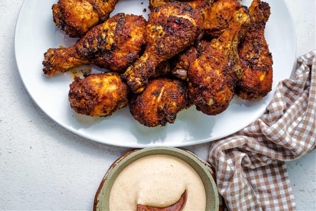 a bowl of Alabama white BBQ sauce in the foreground with a platter of chicken legs in the background.