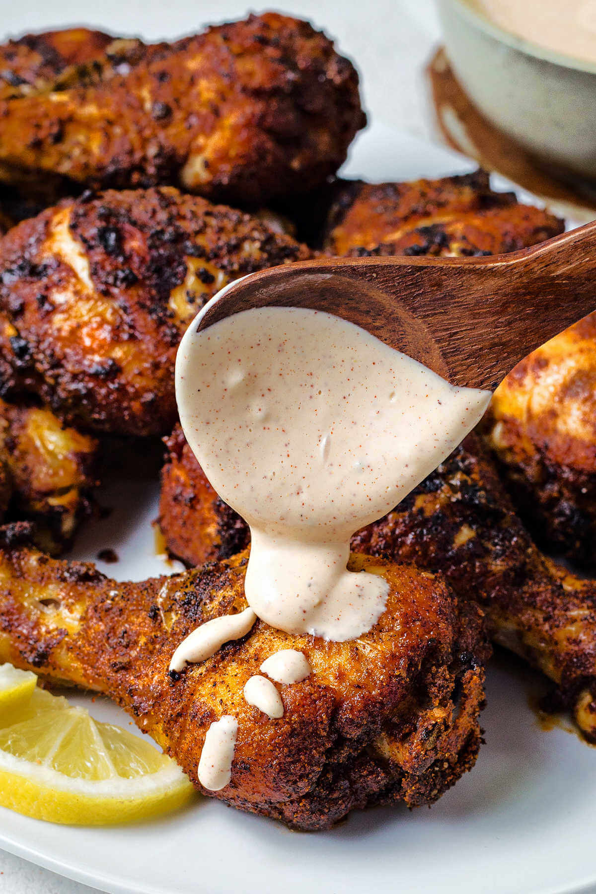 drizzling Alabama white BBQ sauce over a platter of chicken legs.