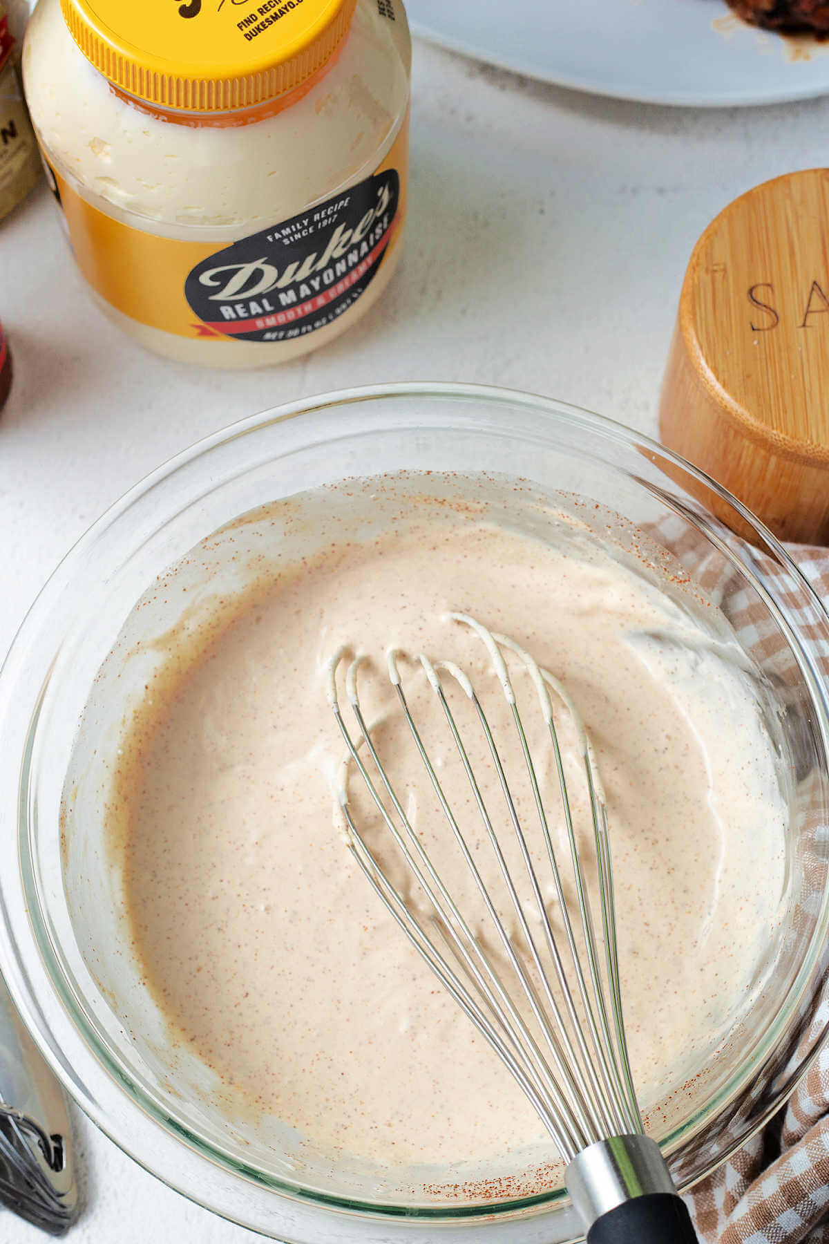 a whisk in a bowl of Alabama white sauce on a table .