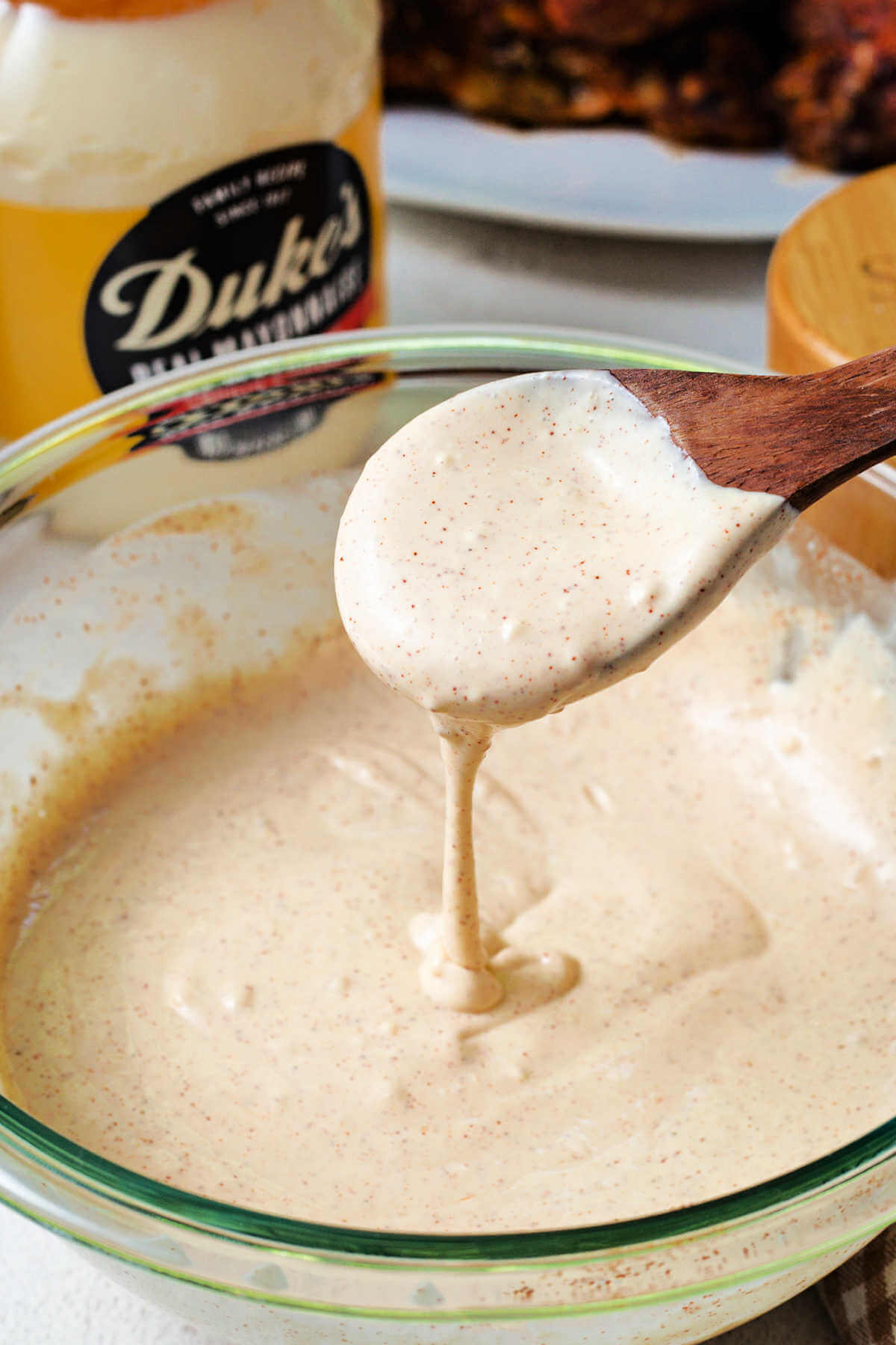 a wooden spoon stirring Alabama white sauce in a bowl.