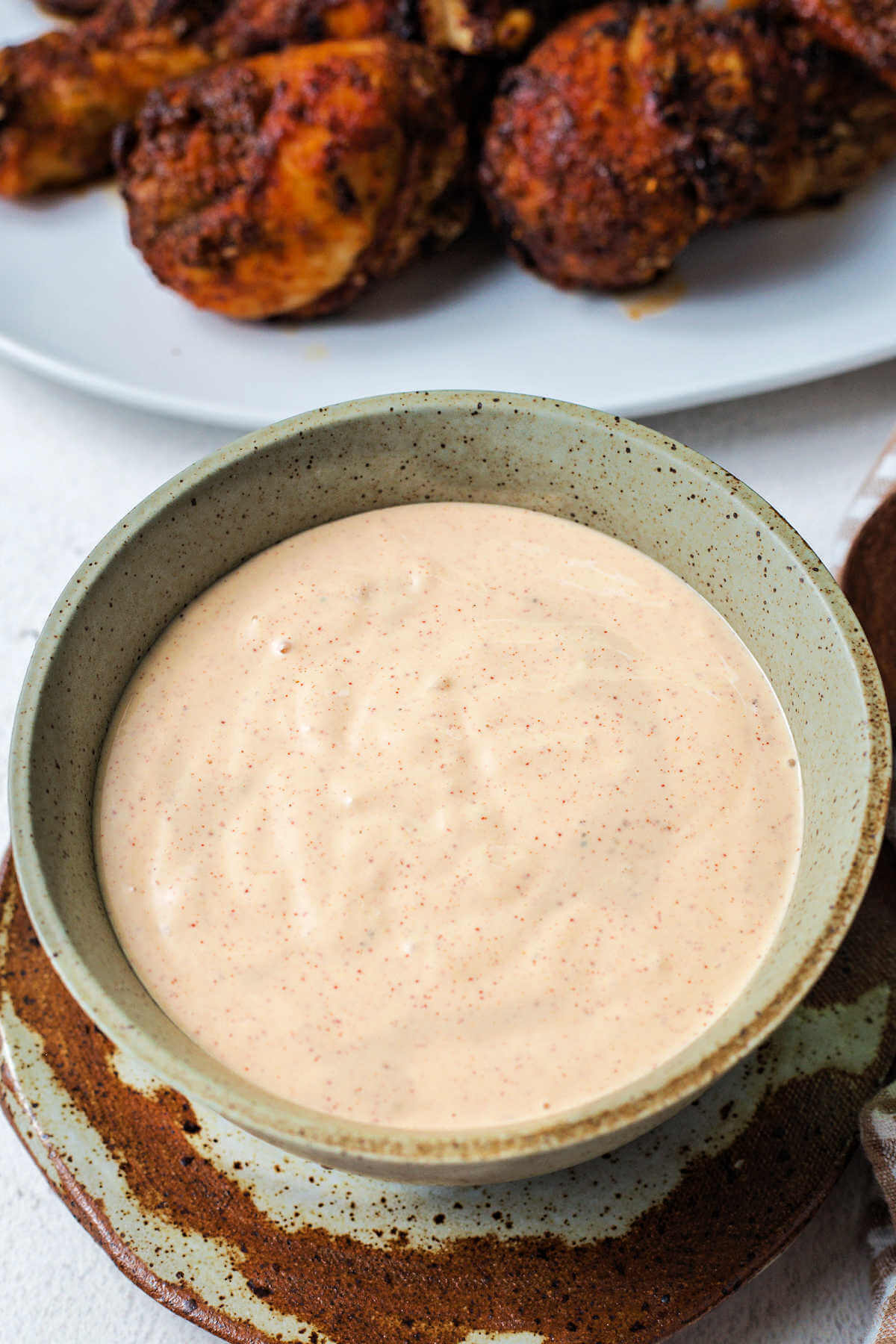 a bowl of Alabama white BBQ sauce on a table with a platter of chicken to the side.