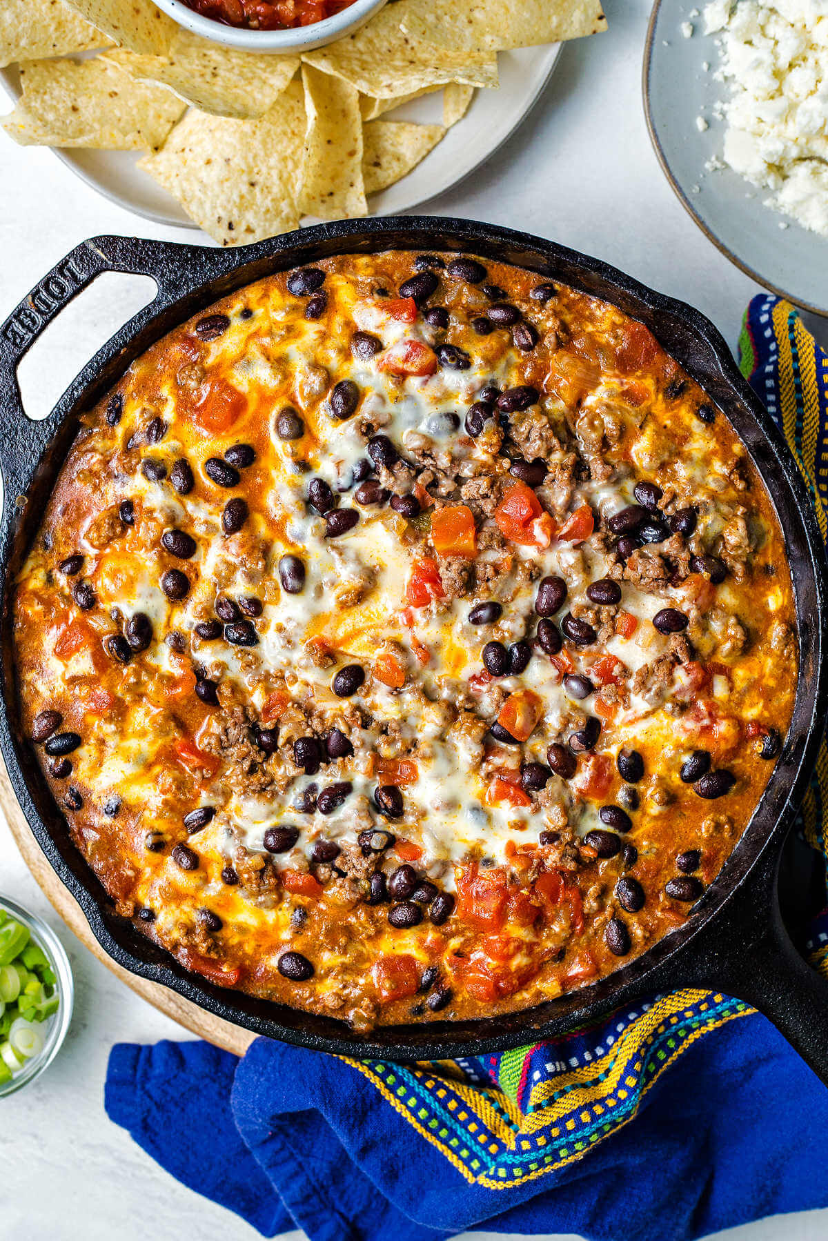 Beef enchilada skillet casserole in a cast iron skillet on a table with a plate of chips and salsa.
