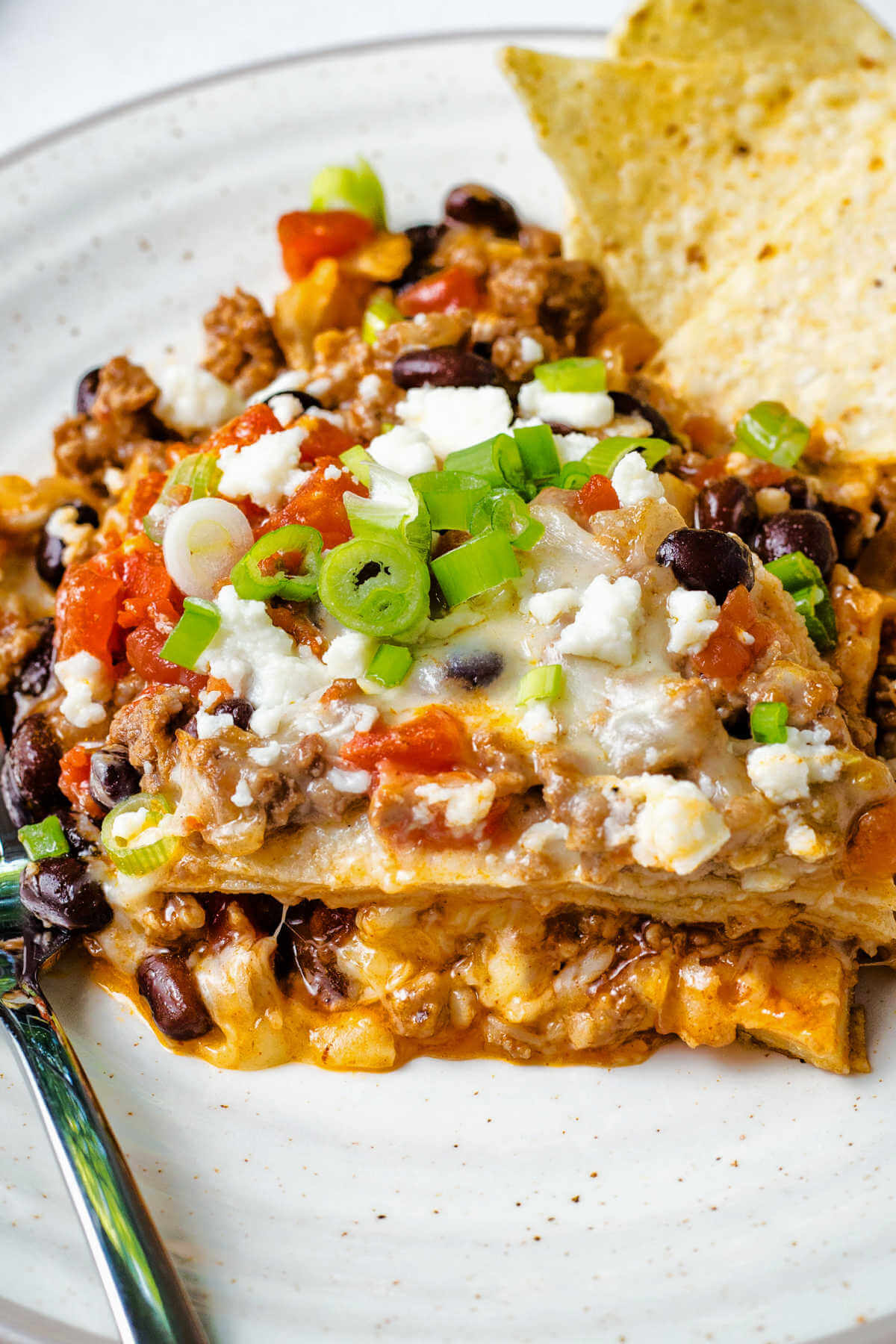a serving of beef enchilada casserole on a plate with a fork and tortilla chips.