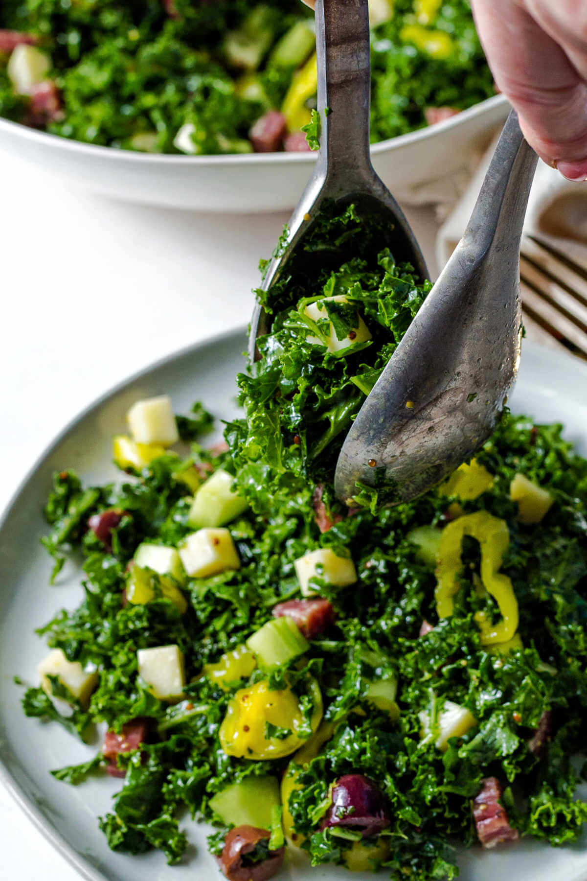 using salad tongs to place a serving of chopped kale salad on a plate.