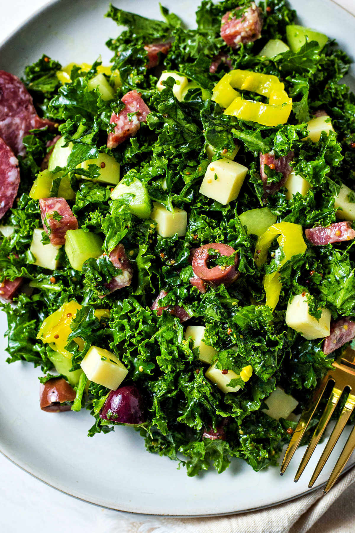 chopped kale salad on a serving plate with a gold fork to the side on a table.