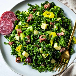 chopped kale salad on a serving plate with a linen napkin and a gold fork to the side on a table.