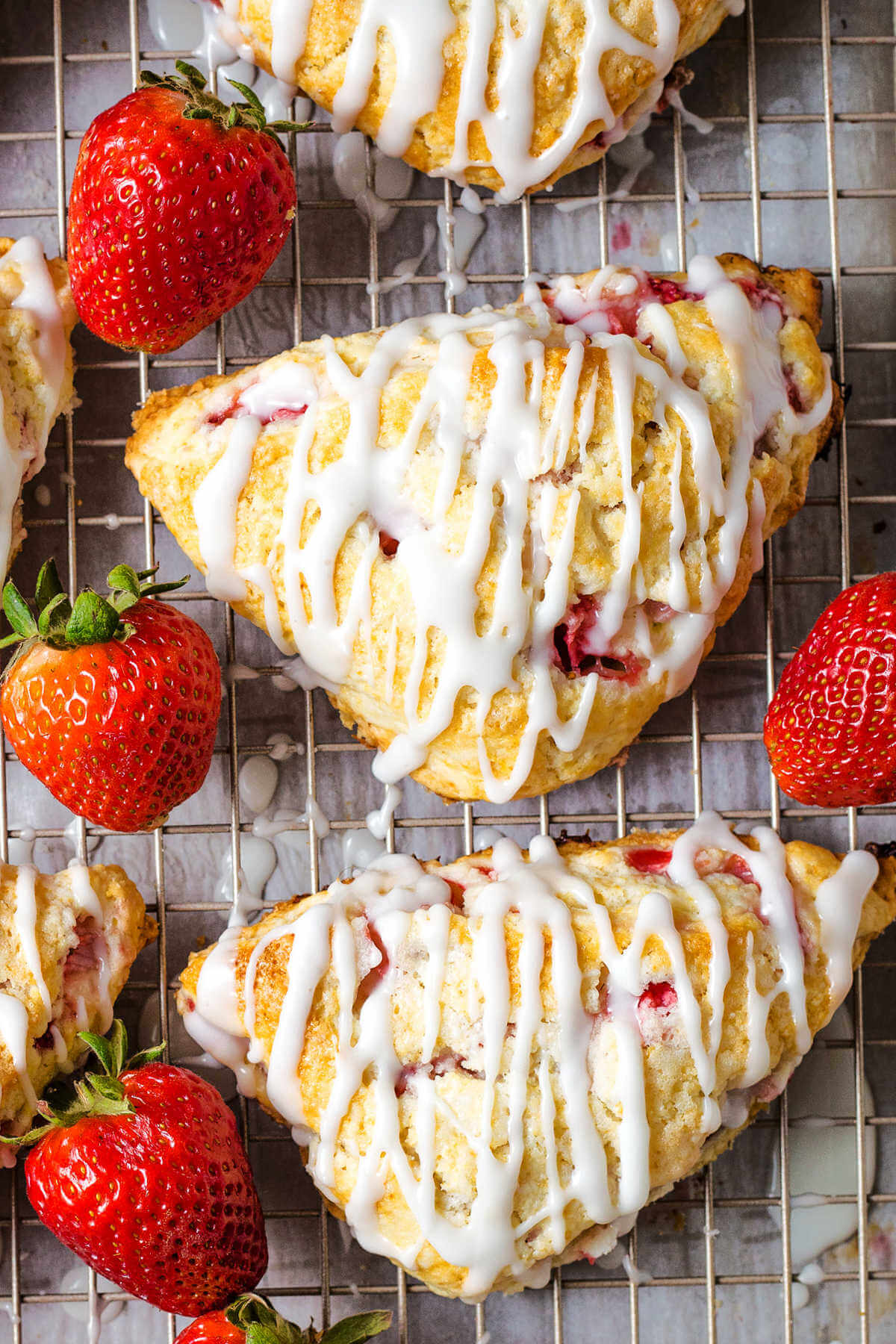 lemon glazed strawberry scones on a wire rack with whole strawberries scattered around.