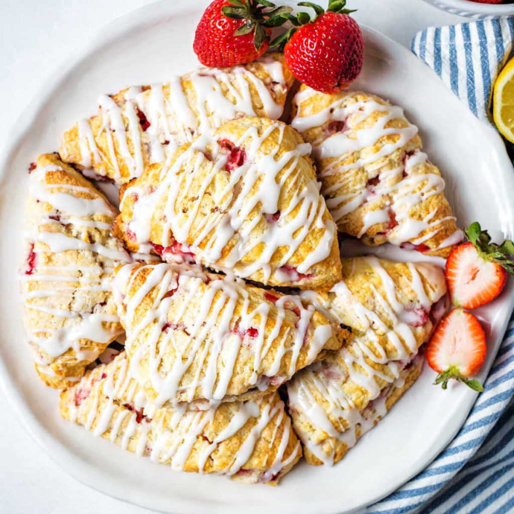 a plate of fresh strawberry scones on a table with a bowl of berries in the background.