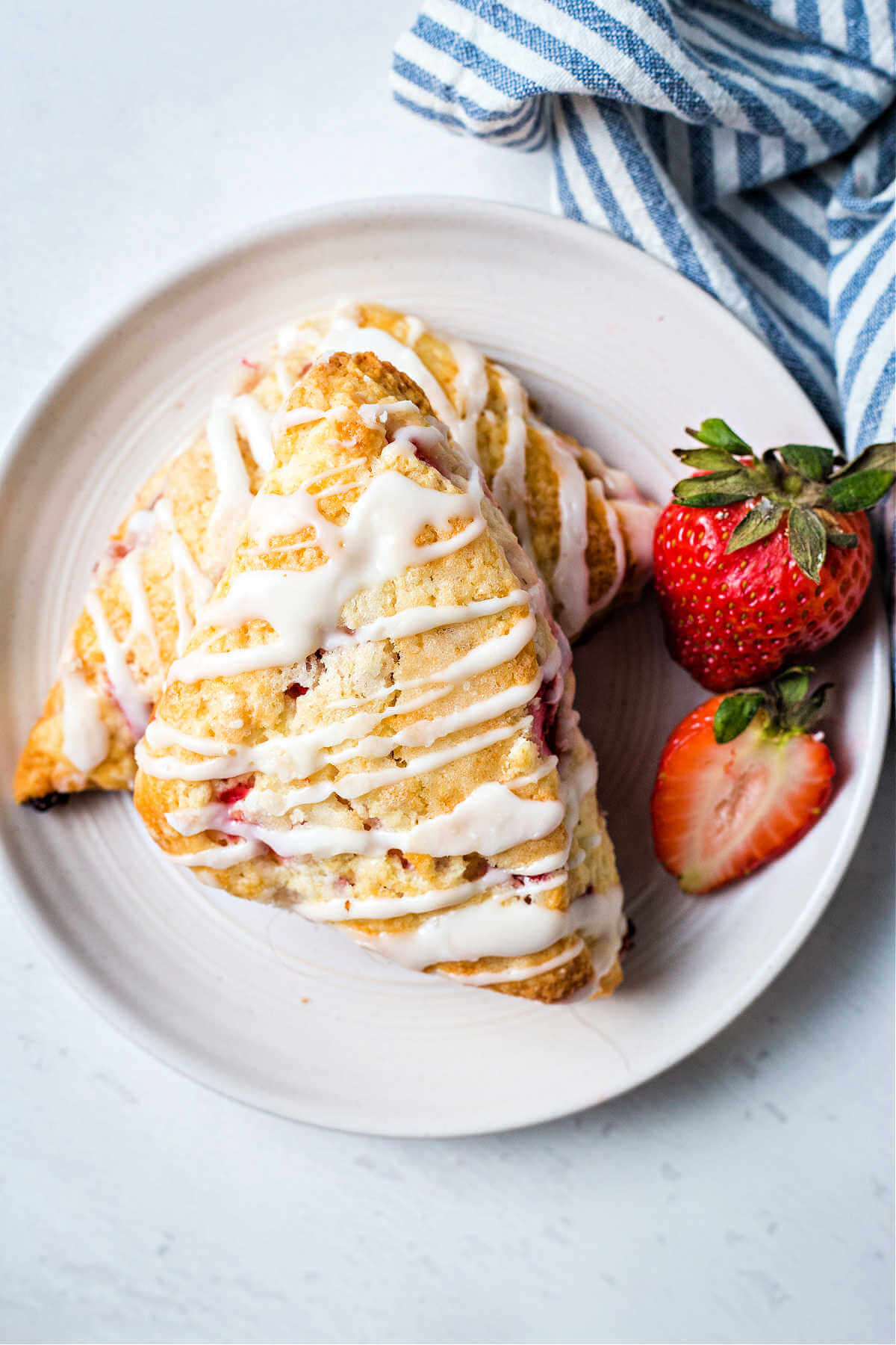 two strawberry scones on a white plate with a whole strawberry to the side on a table.