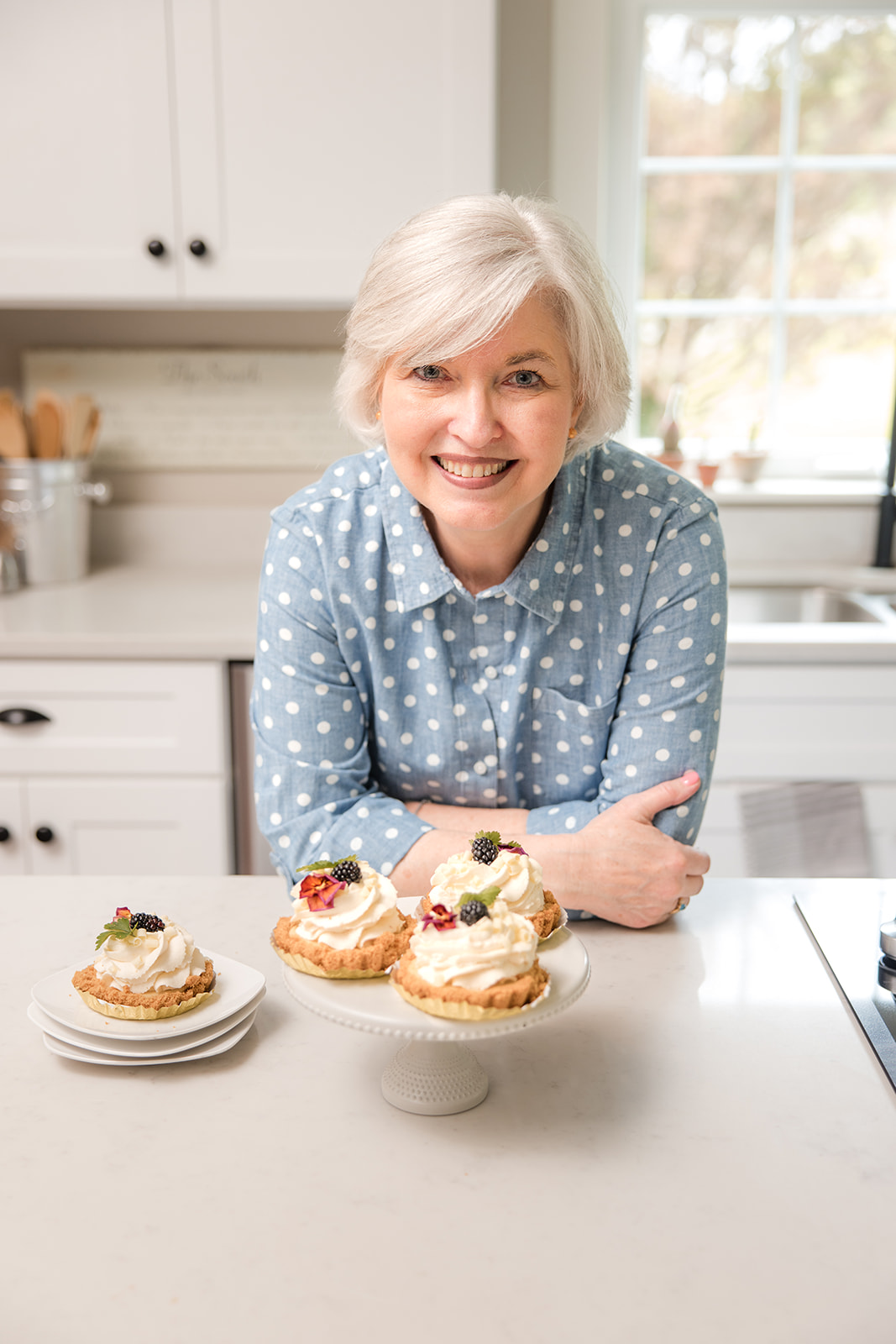 Sheila Thigpen leaning against a kitchen island with dessert on a pedestal.