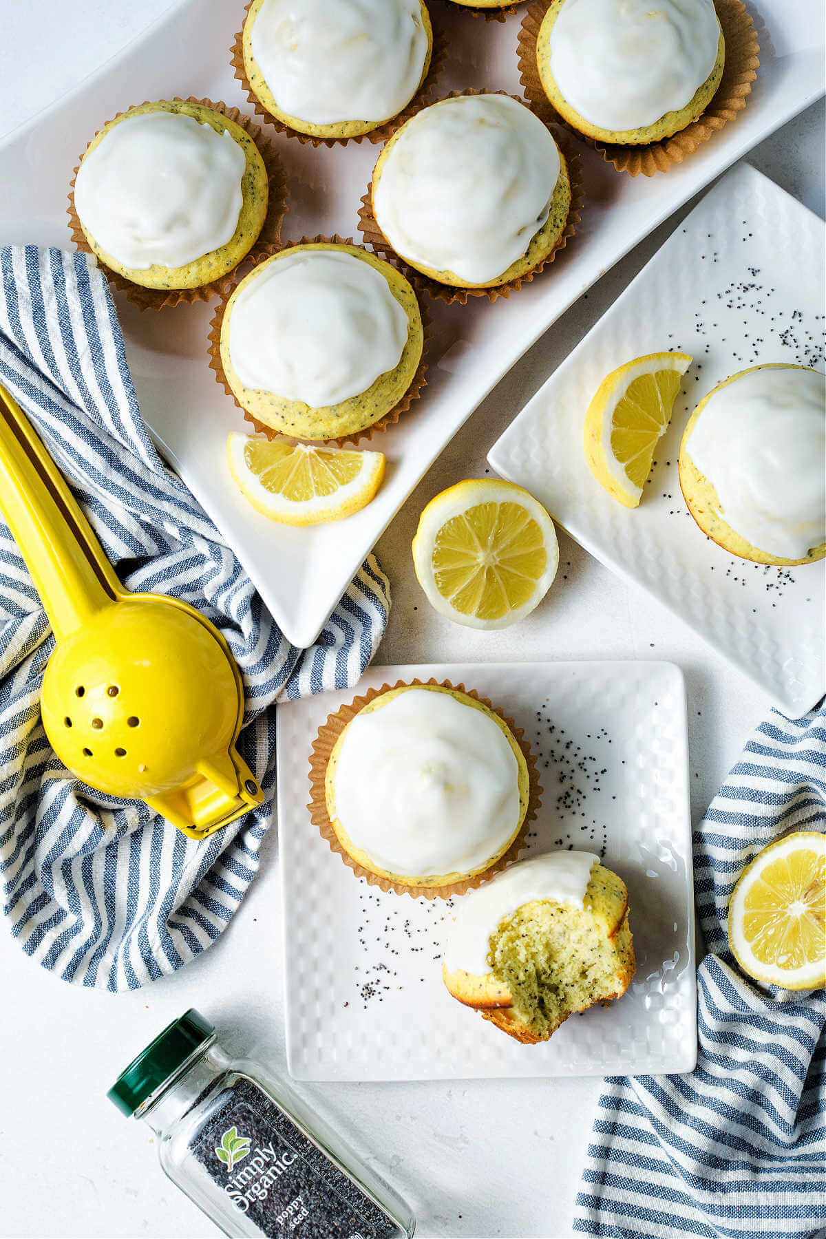 a tray of lemon poppyseed muffins on a table with a citrus press, jar of poppyseeds and lemon slice.