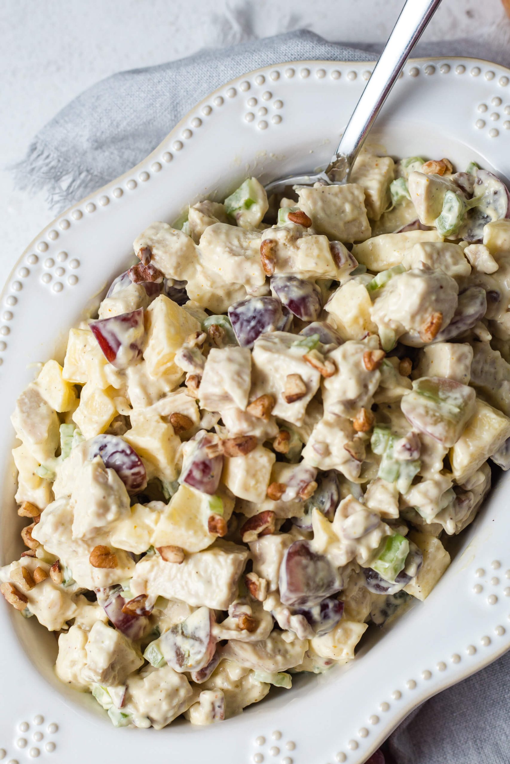 Southern chicken salad with grapes and pecans in a decorative white bowl with a serving spoon on a table.