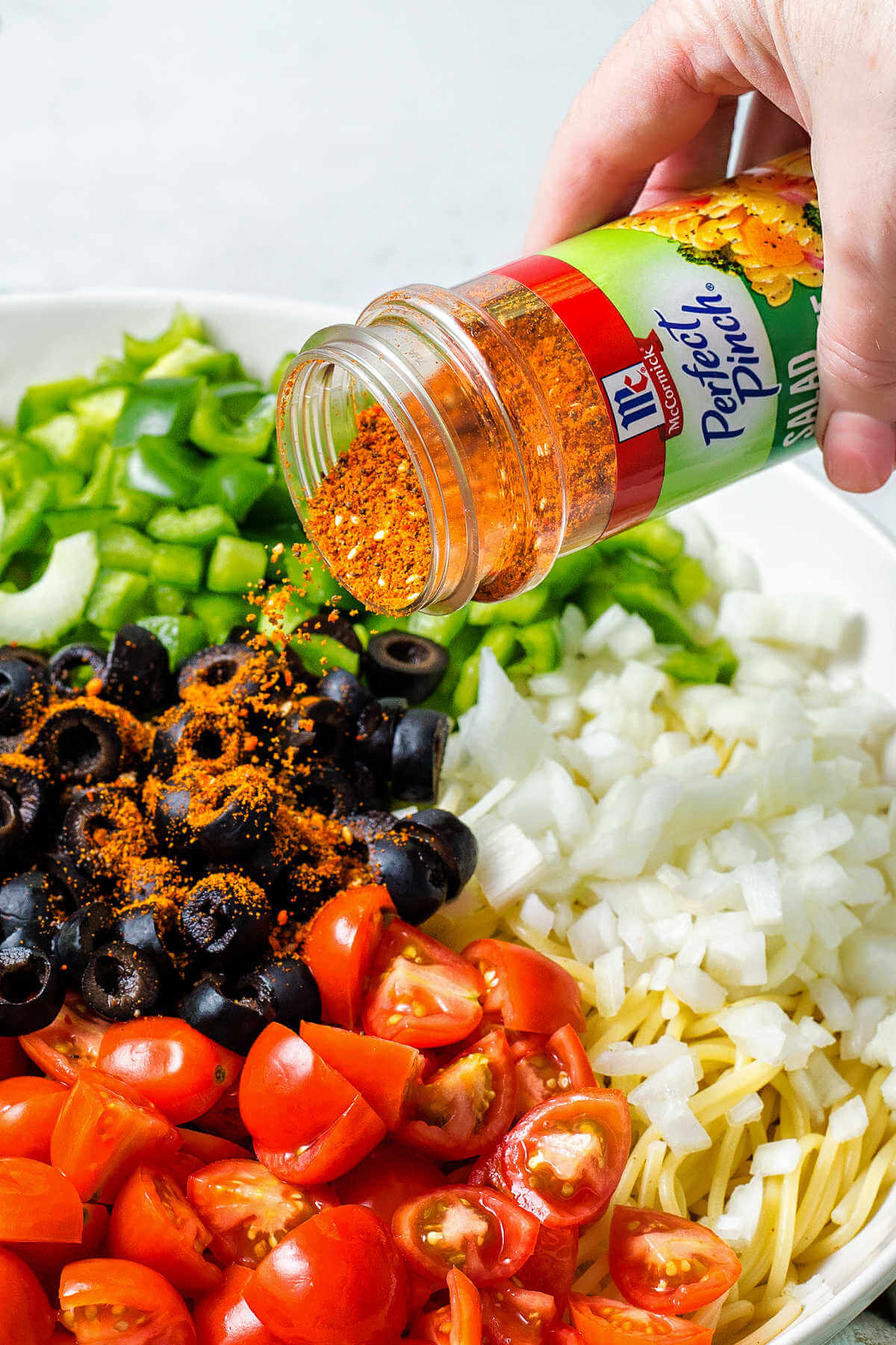 sprinkling McCormick's Salad Supreme seasoning on top of vegetables in a bowl.