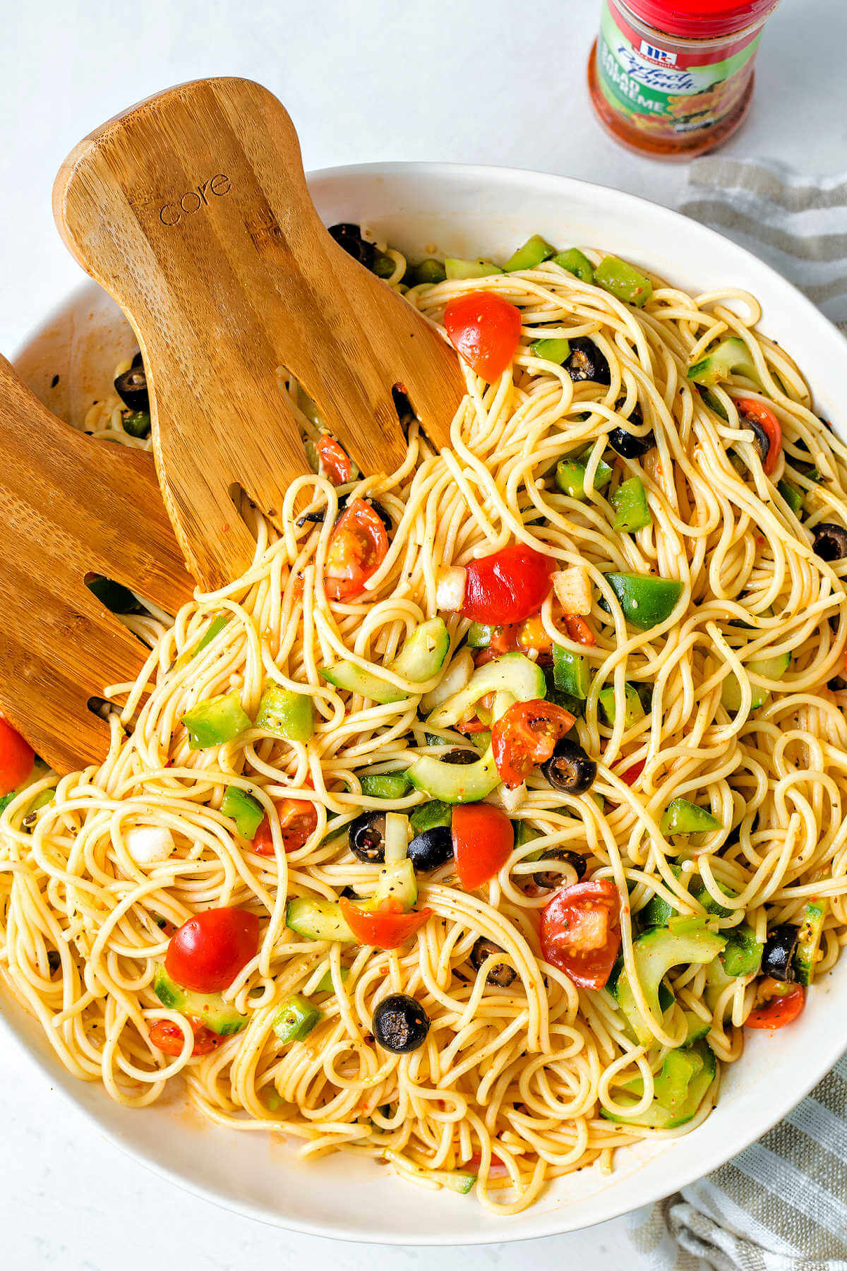ingredients tossed together in a bowl with wooden salad tongs for spaghetti pasta salad.