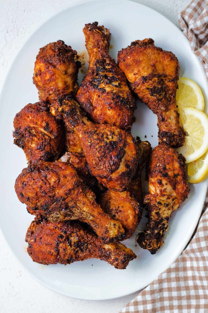 air fryer chicken legs piled high on a white platter and garnished with lemon slices.