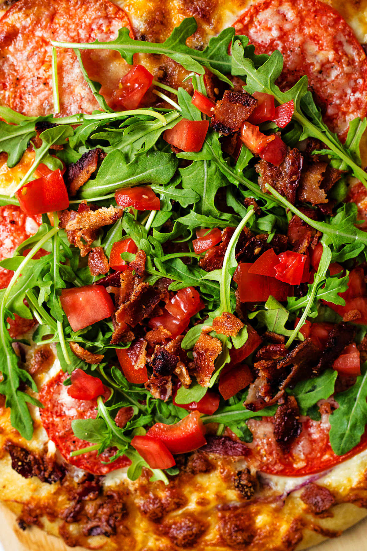 BLT pizza topped with baby arugula, bacon, and chopped tomatoes.
