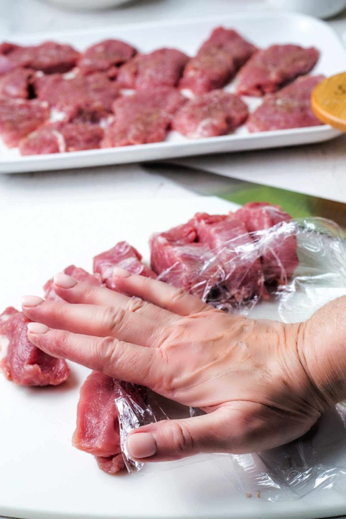pressing pork medallions flat with the palm of a hand.