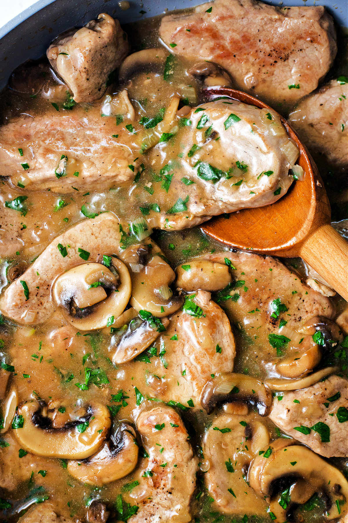 simmering pork medallions with mushroom gravy in a skillet with a wooden spoon.