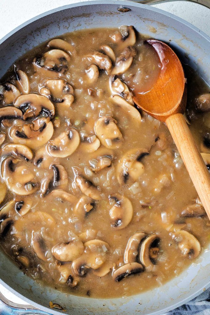 stirring mushroom gravy with a wooden spoon for pork medallions.