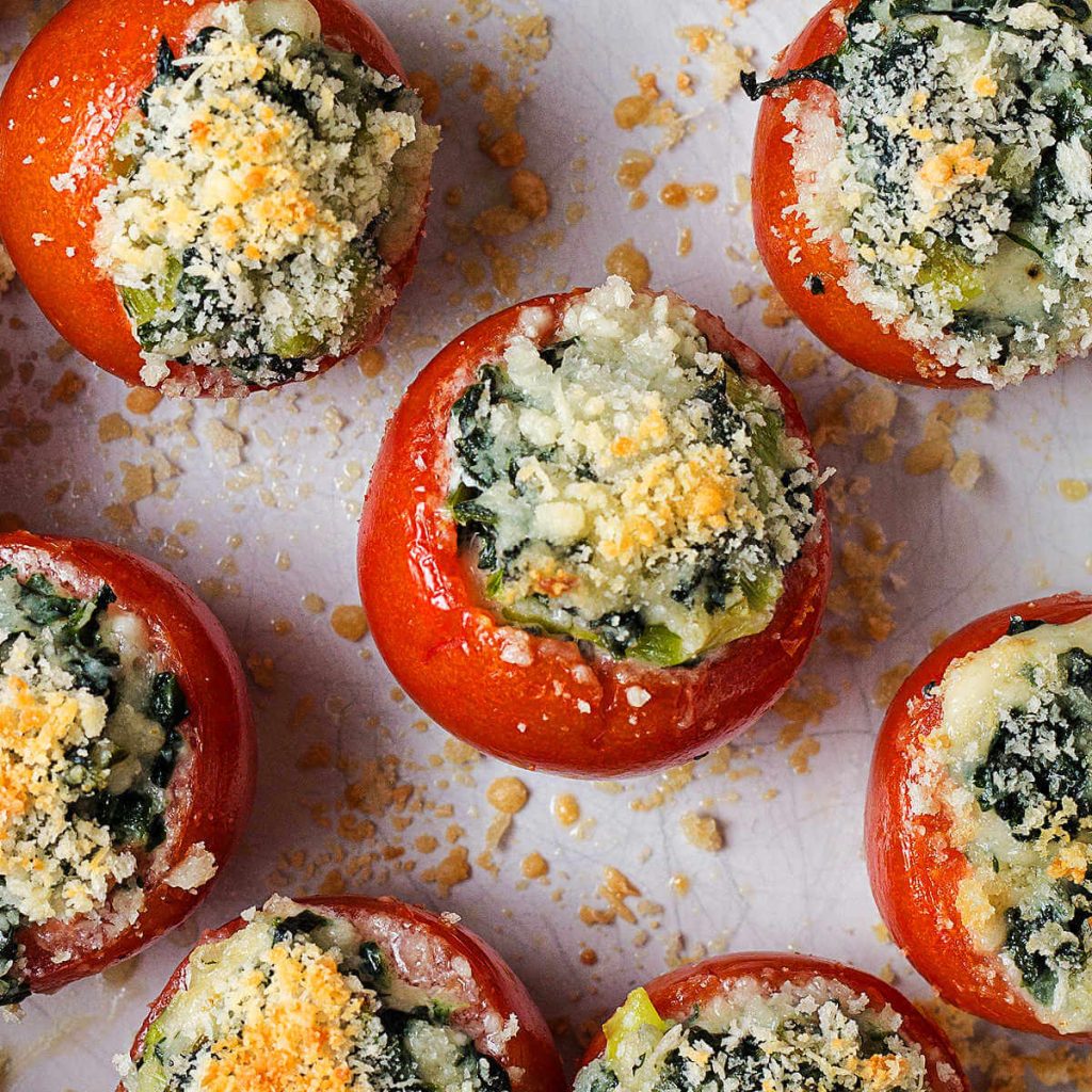 spinach stuffed baked tomatoes with panko breadcrumbs toasted on top in a baking dish sitting on a croqueted trivet.