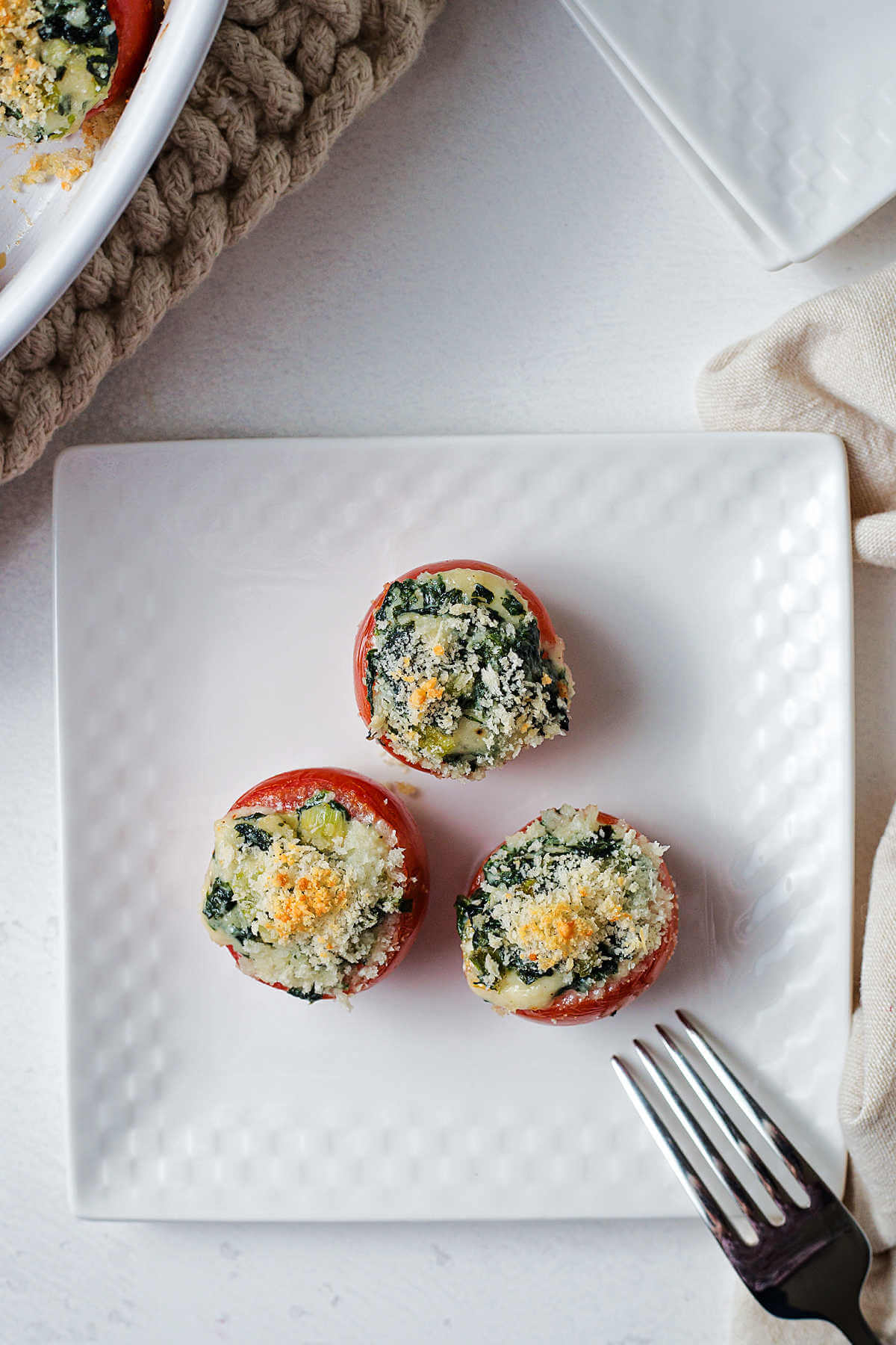 three spinach stuffed tomatoes on a white plate with a fork.