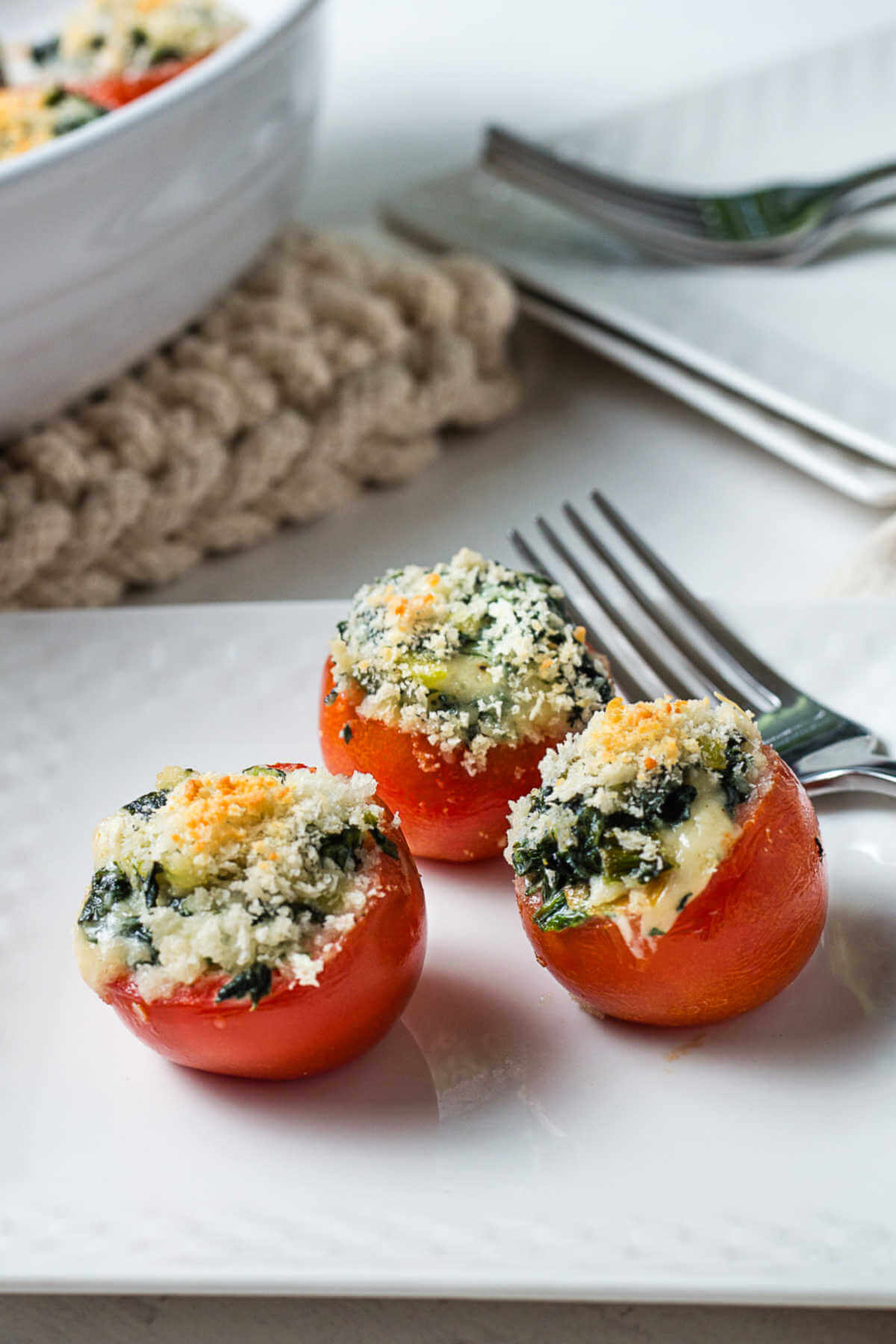 three spinach stuffed tomatoes on a white plate with a fork.