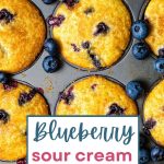 Blueberry Sour Cream Muffins in a muffin pan with fresh blueberries.