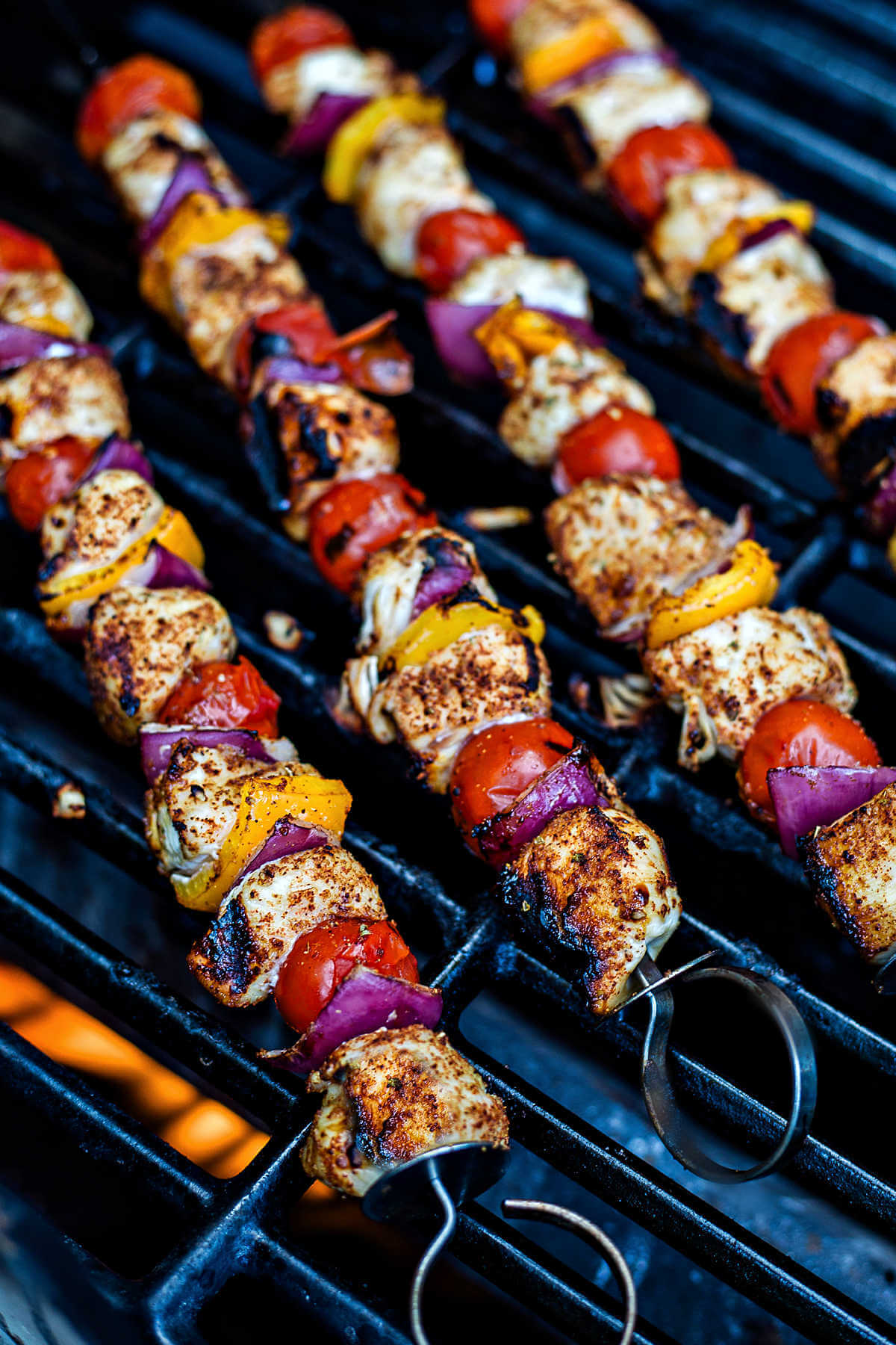 chicken skewers cooking on a gas grill.