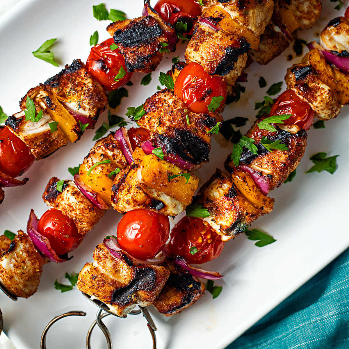 grilled chicken kabobs on a plate with parsley sprinkled around.