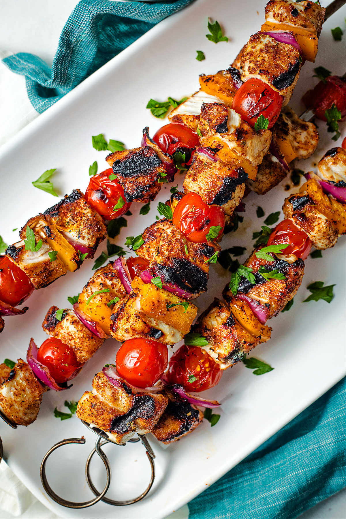 grilled chicken kabobs on a plate with parsley sprinkled around.