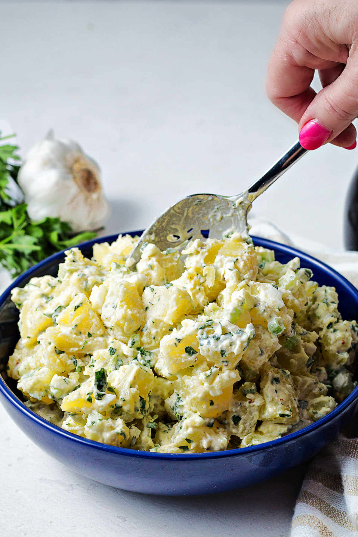 spooning potato salad into a blue serving bowl on a table.