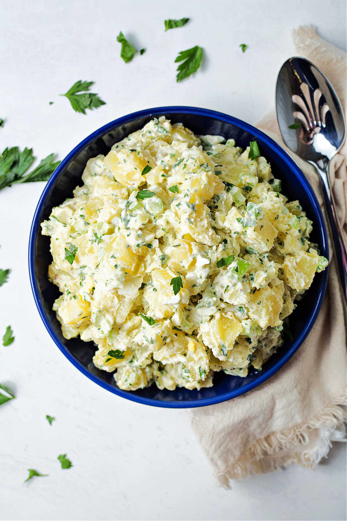 fresh herb potato salad in a blue bowl on a table with a linen napkin and a serving spoon.