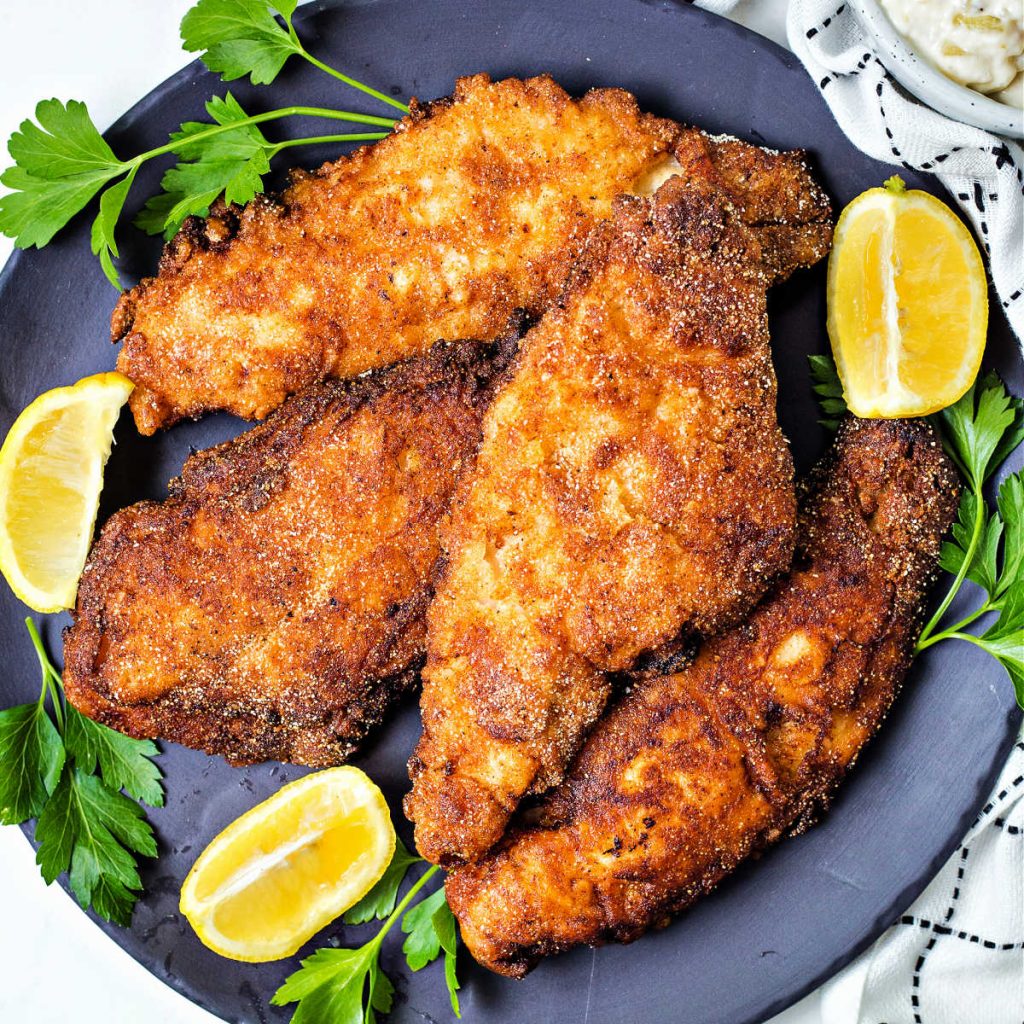 fried catfish on a plate with lemon wedges