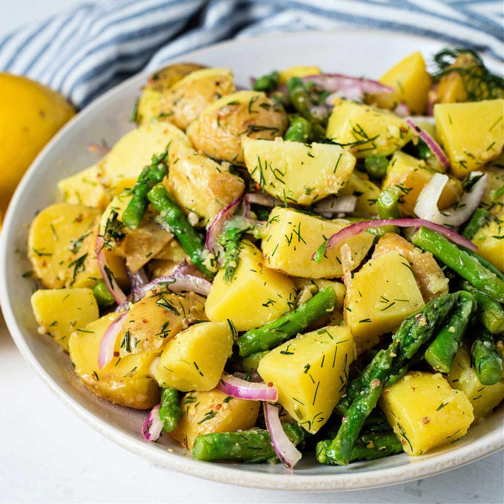 lemon dill potato salad with asparagus in a white bowl on a table.