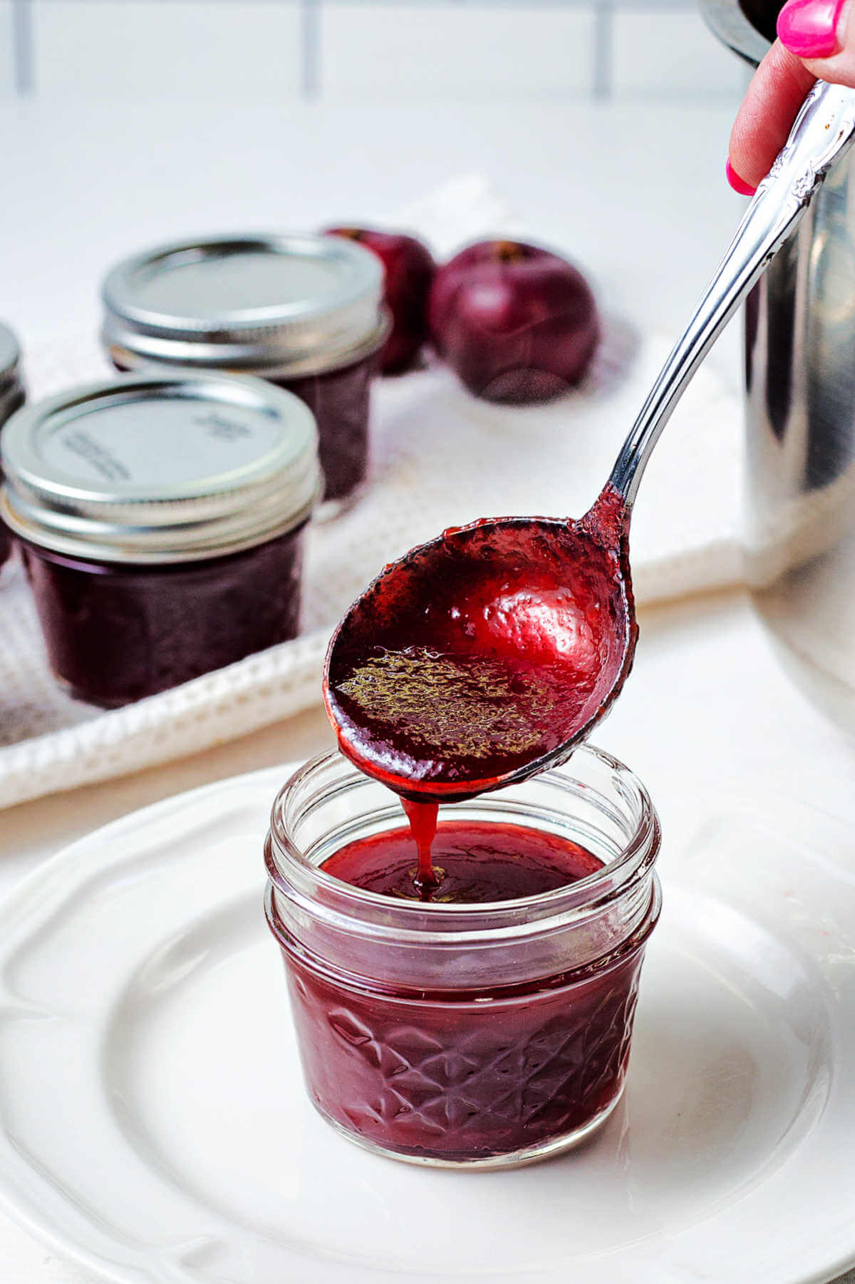 spooning plum jam into a glass jar for canning.