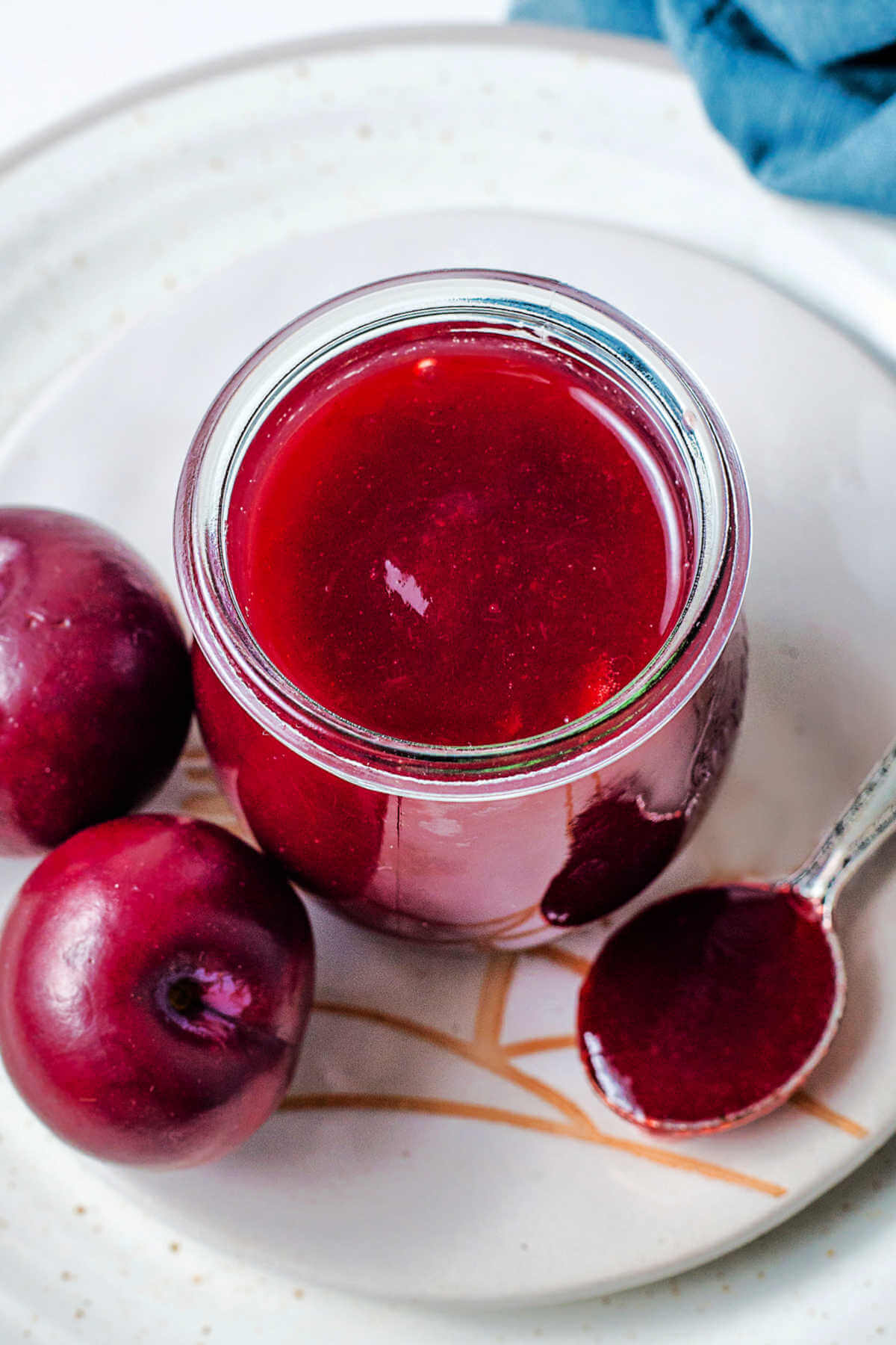 a jar of plum jam on a plate with a spoon and whole plums.