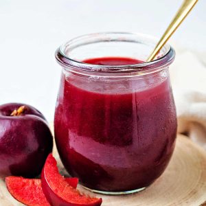 a jar of plum jam with a spoon inserted.