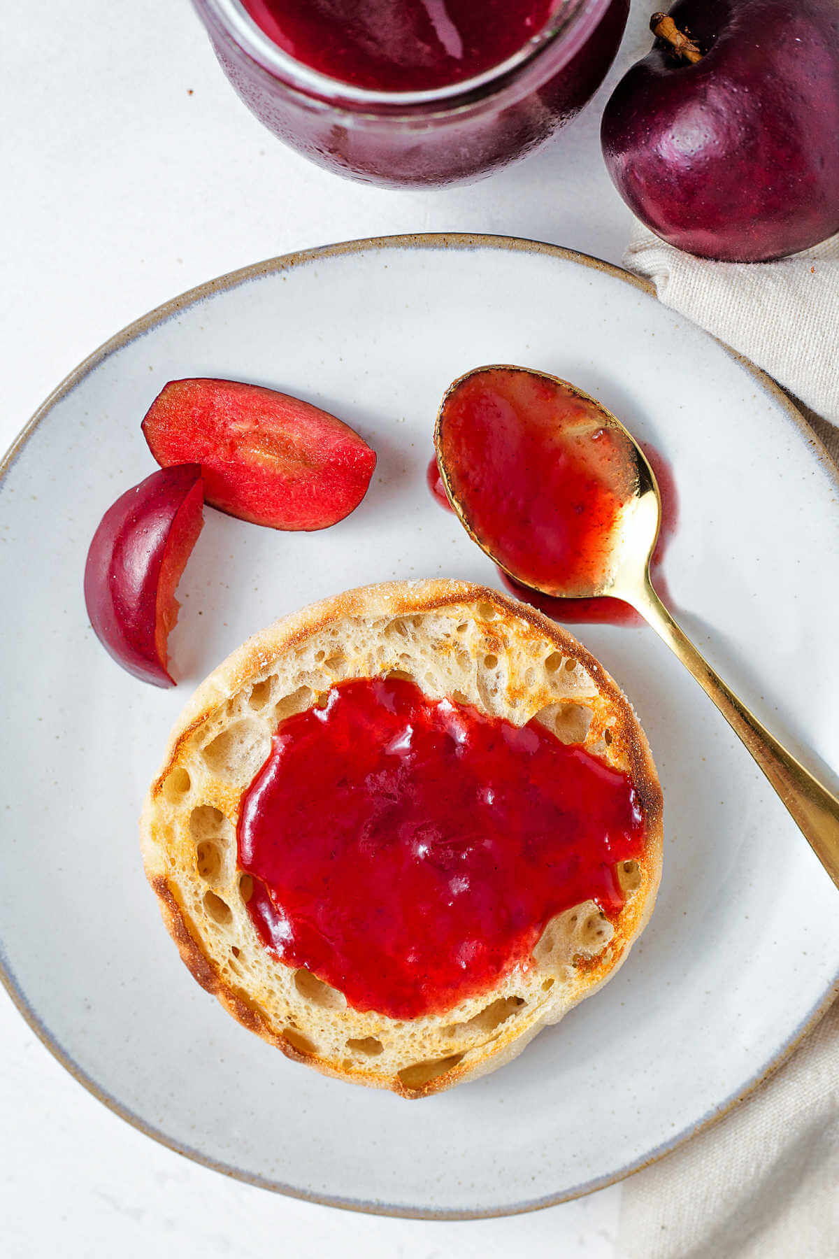 plum jam spread on an English muffin on a plate.