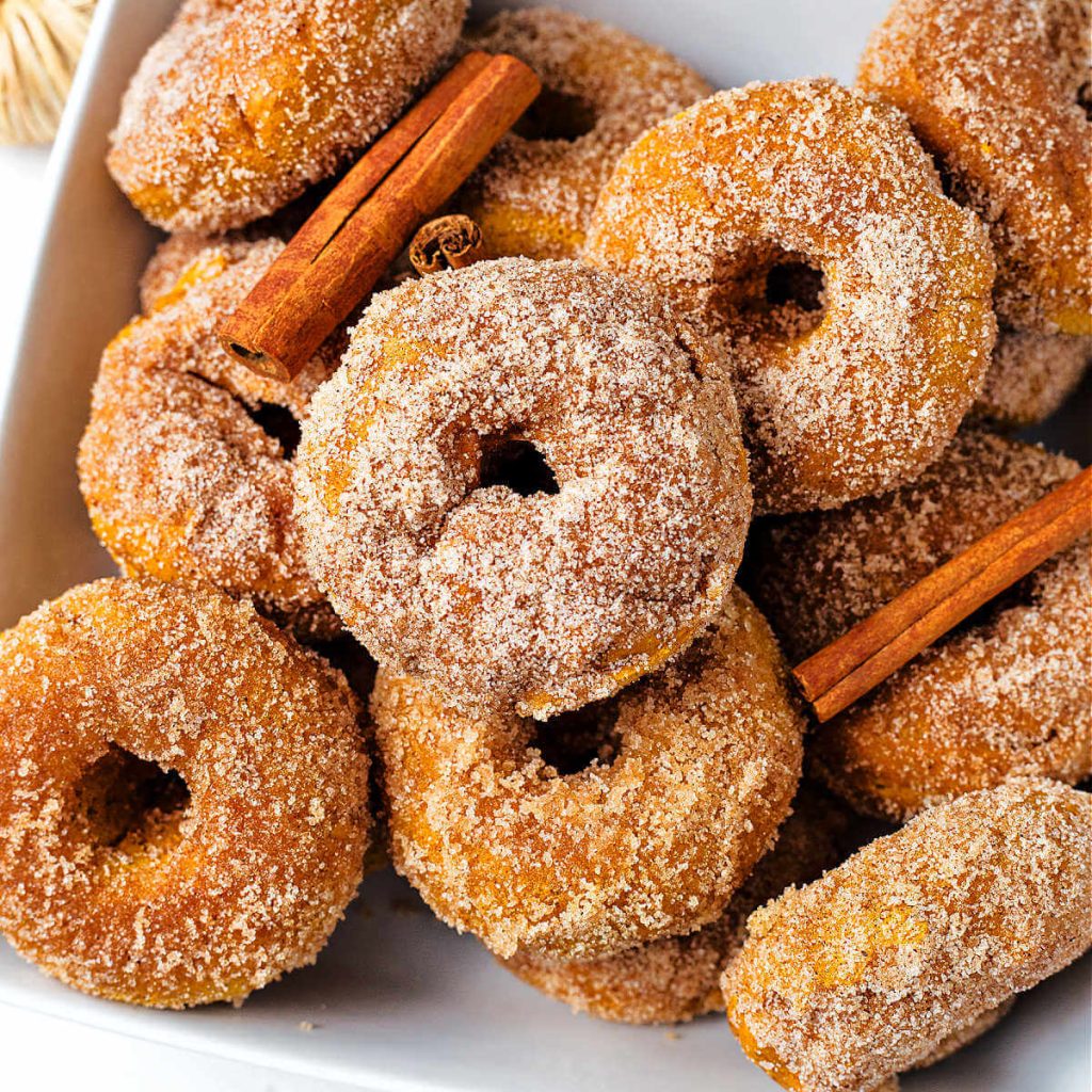 baked pumpkin donuts stacked in a bowl with cinnamon sticks.