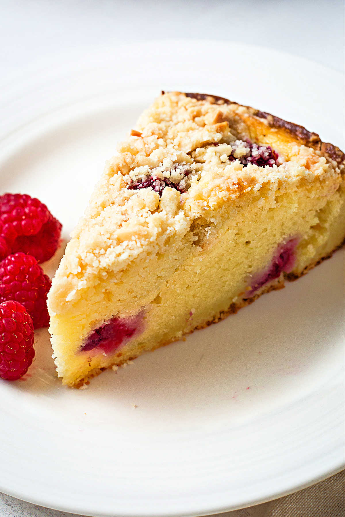 close up of a slice of raspberry ricotta cake with an almond streusel topping on a plate.