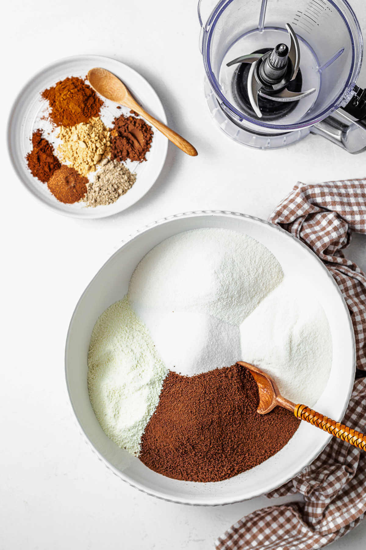 ingredients for chai tea mix in a bowl with a spoon, with a plate of spices on the table.