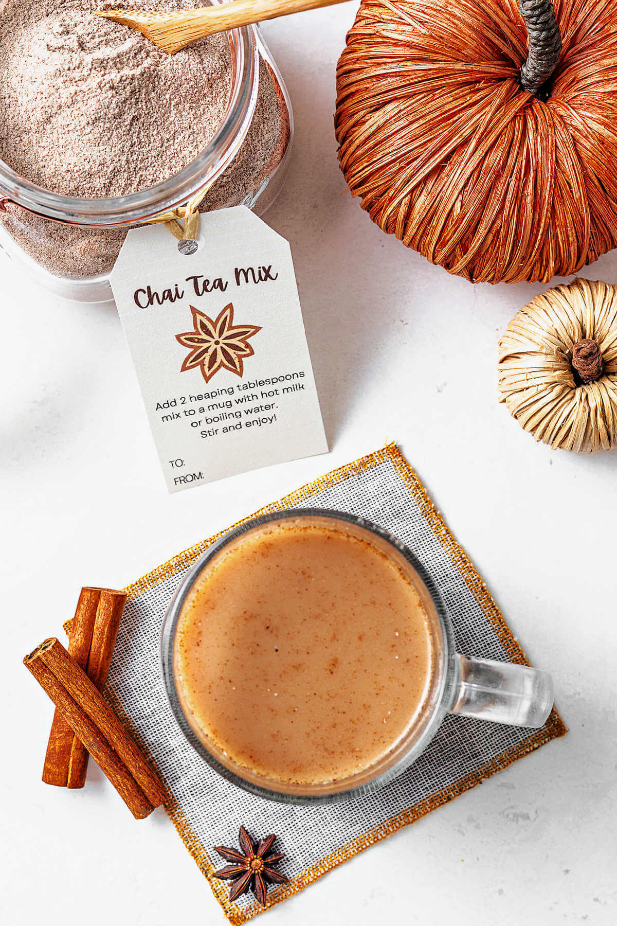 chai latte tea mix in a glass jar with a gift tag and a cup of chai tea on a coaster on a table.