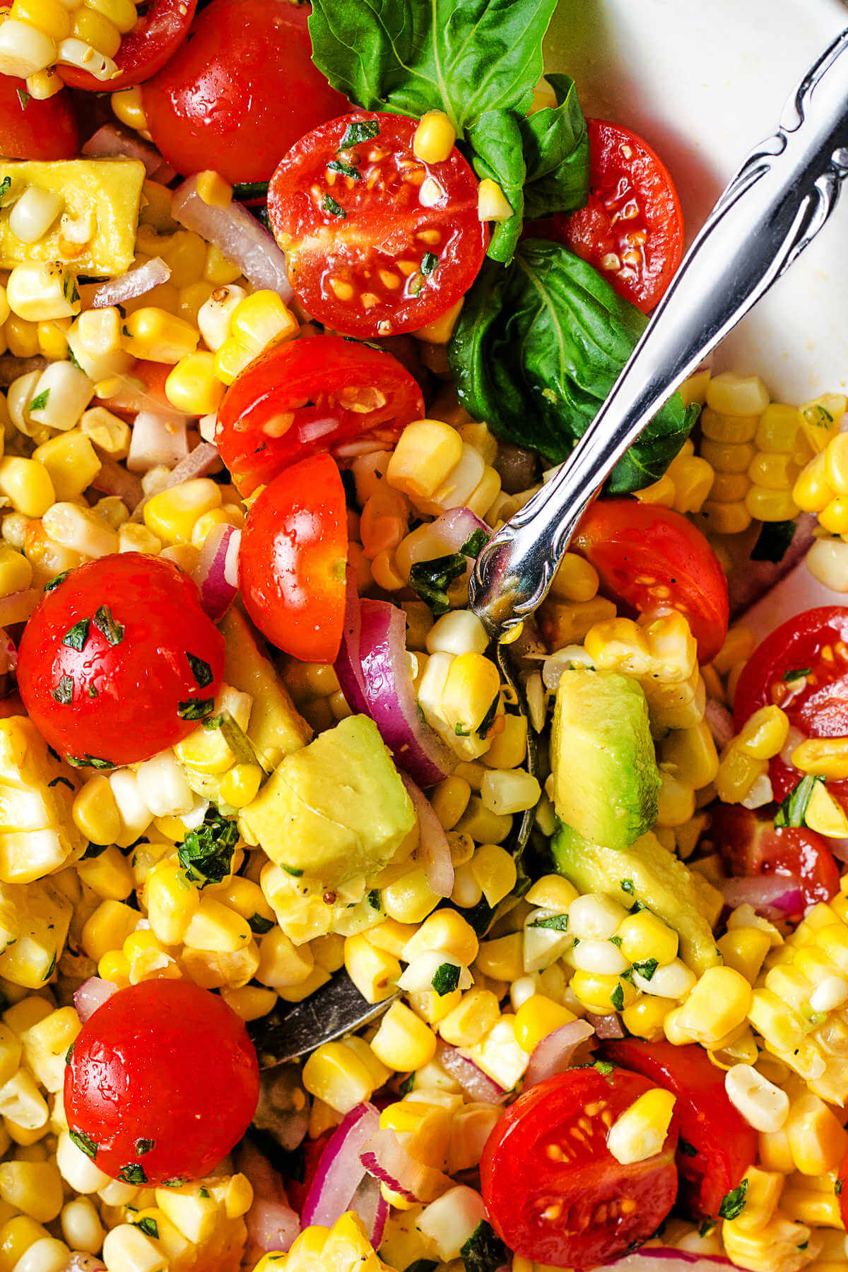 a serving spoon inserted into a bowl of corn and avocado salad.