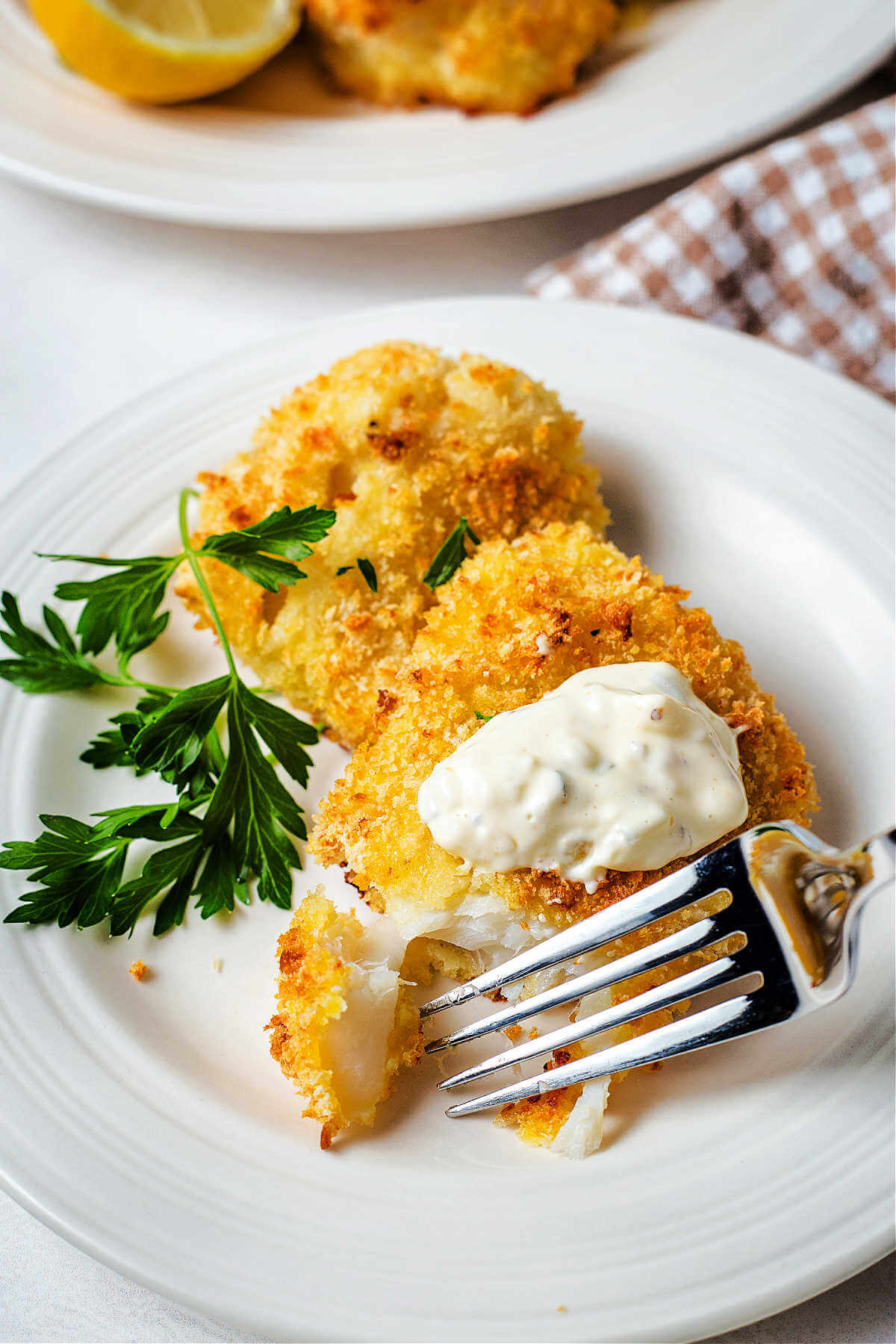 fish topped with tartar sauce being flaked with a fork on a plate.