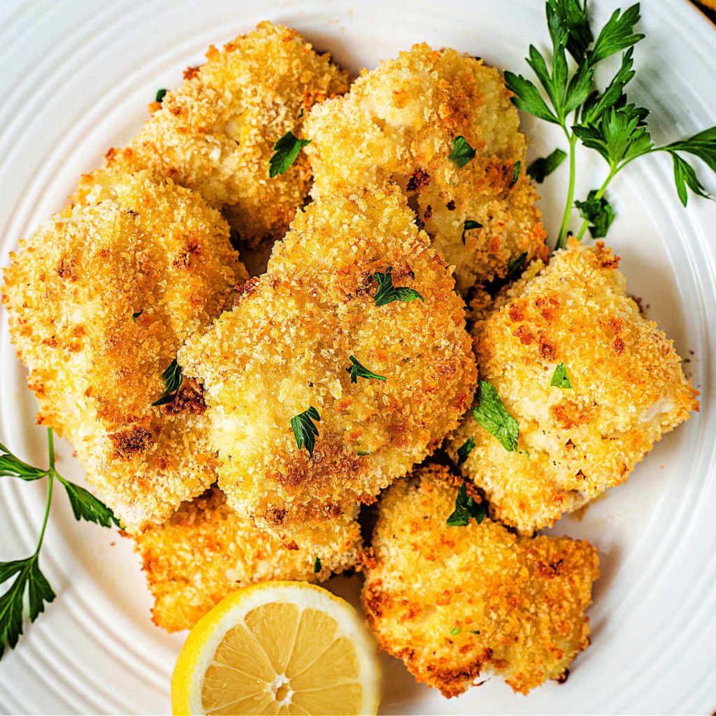 oven fried fish filets on a white plate garnished with parsley and lemon.