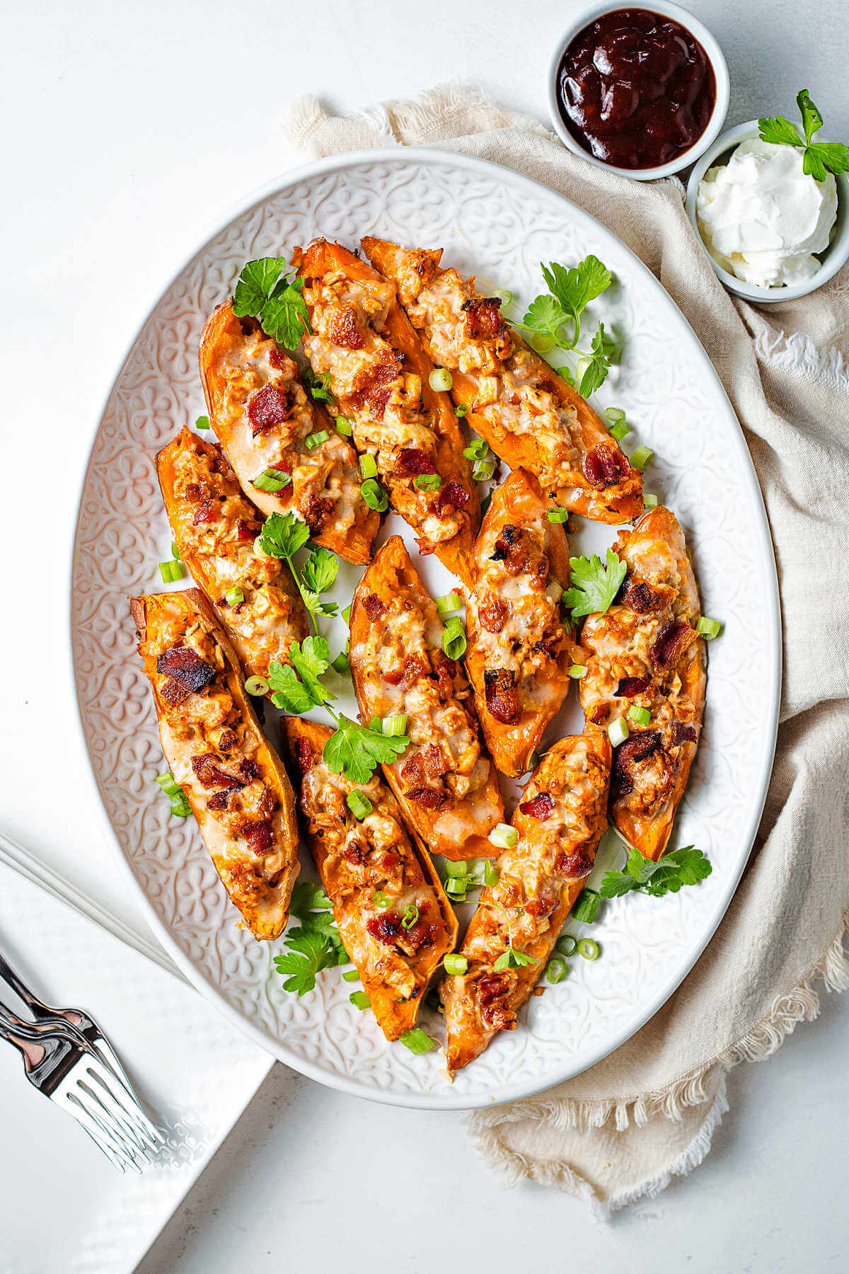 loaded sweet potato skins on a white platter on a table with a bowl of sour cream and bbq sauce.