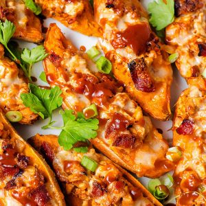 loaded sweet potato skins garnished with bbq sauce, sliced green onions, and parsley.